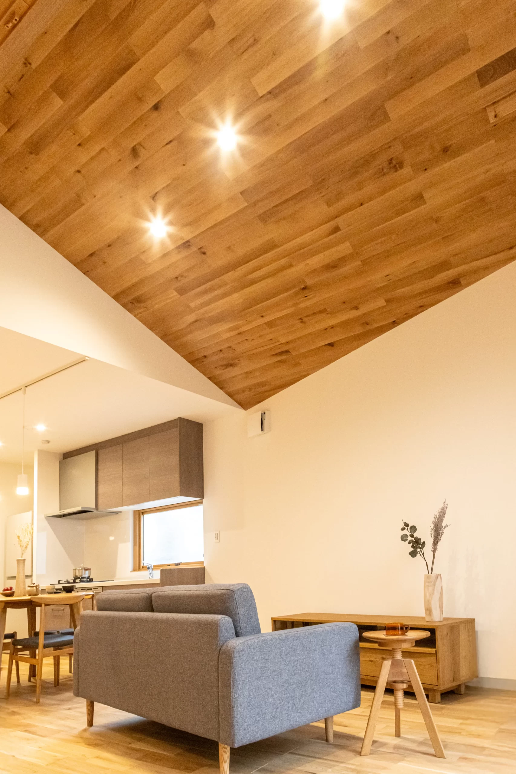 木目張りの勾配天井が特徴的な、グレーのソファを置いた開放的なリビング