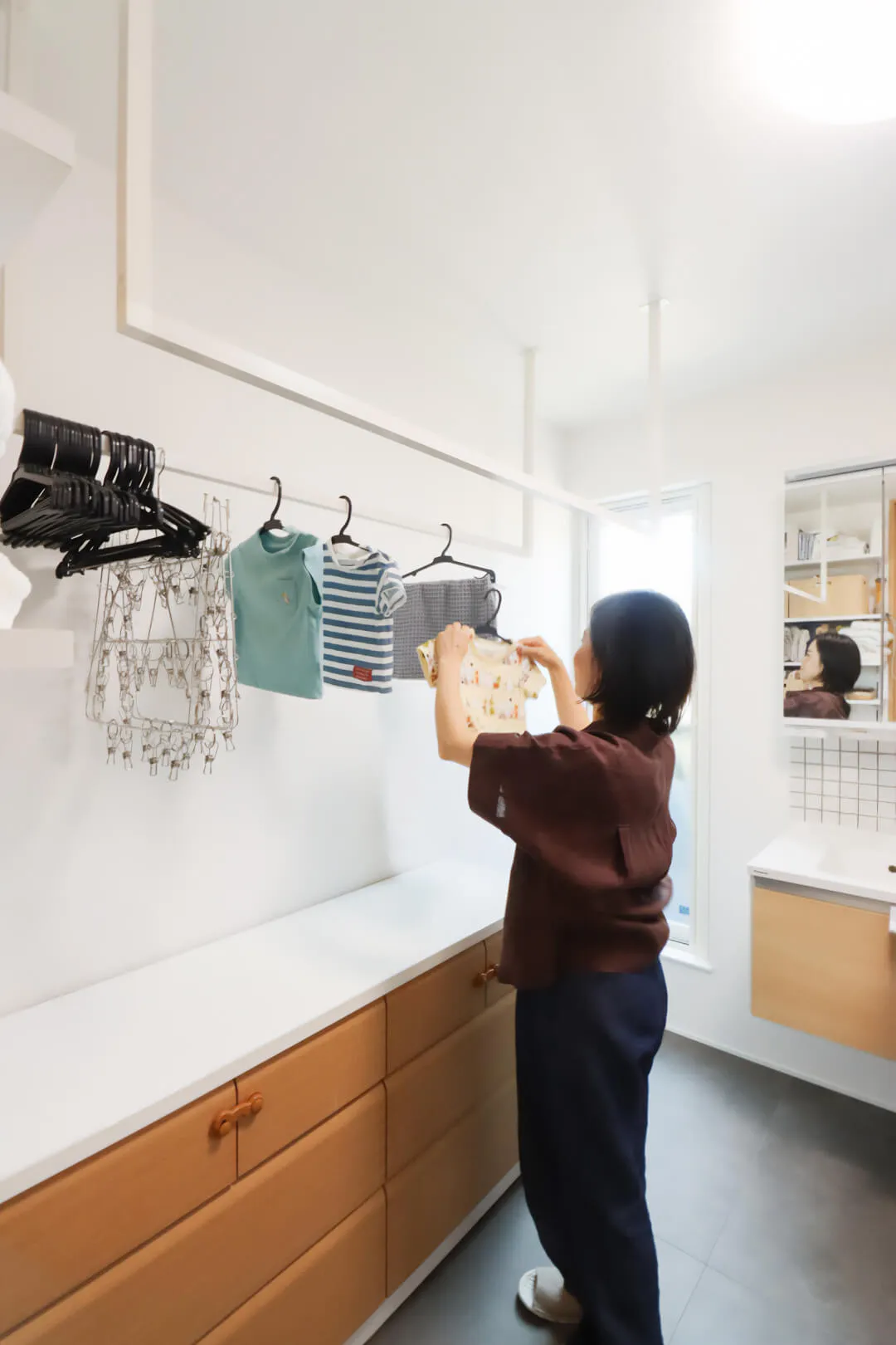 白い壁と木目調の収納がある清潔なランドリールームで洗濯物を干す女性