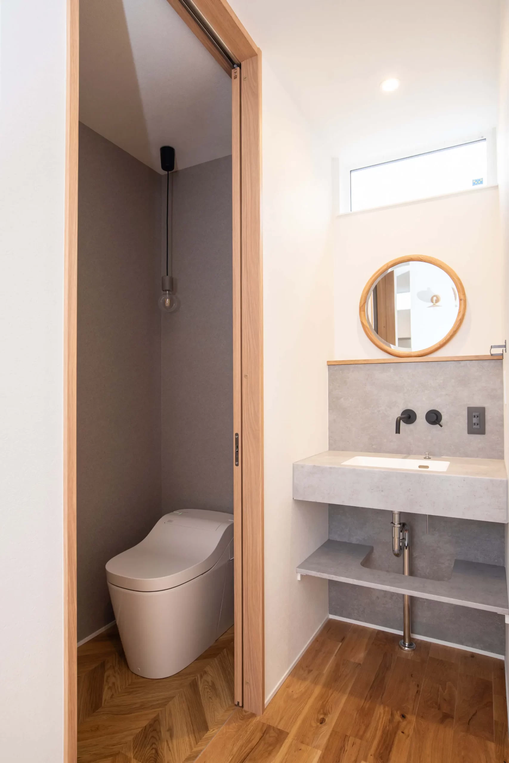 ヘリンボーンの床と木の建具、造作手洗いカウンターがあるトイレ空間