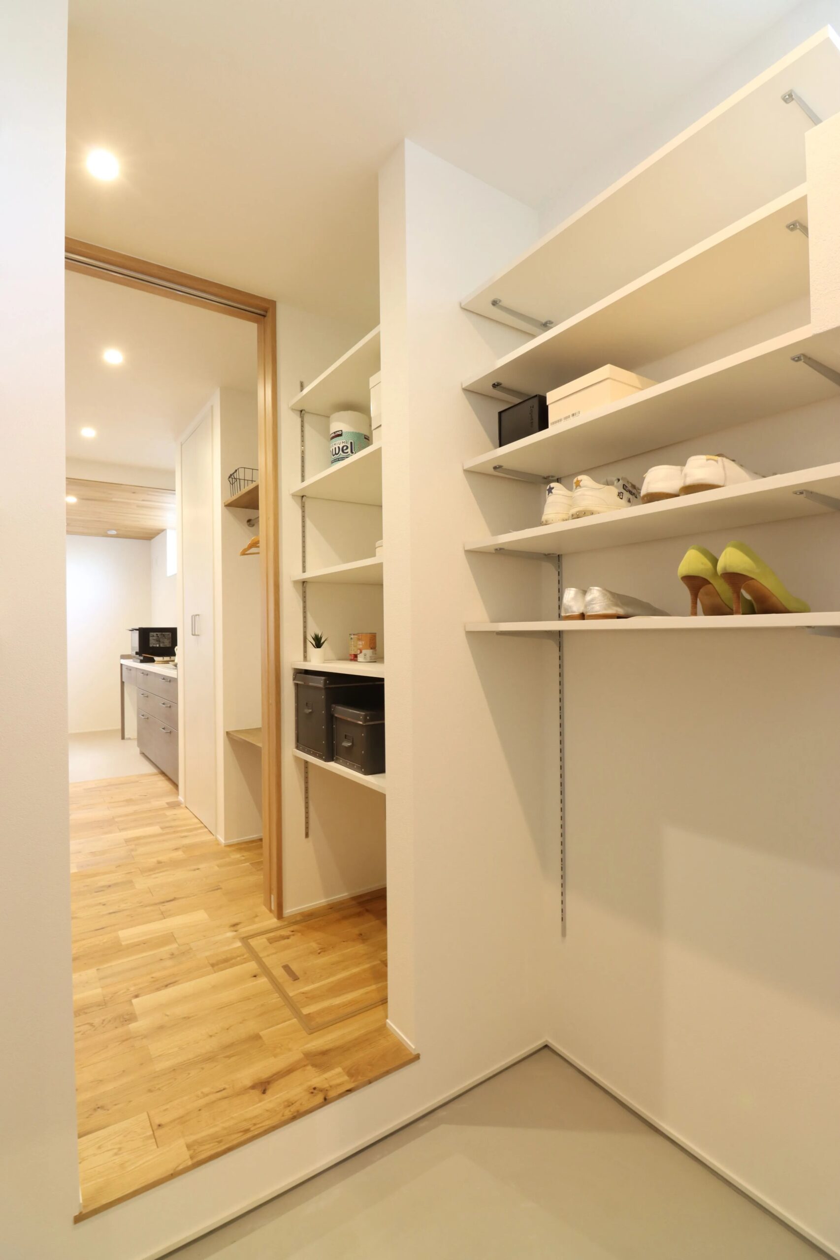 無垢フローリングの廊下と大容量の可動棚を備えたシューズクローク
