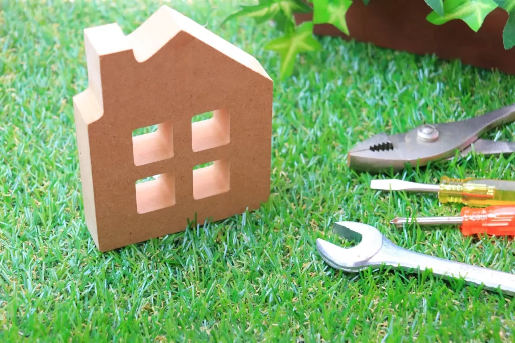 芝生の上で家の模型とペンチなどの工具の写真