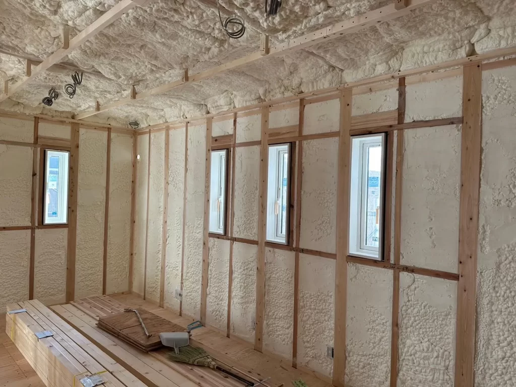 建築中の木造注文住宅の室内において、壁や天井の構造材の間に隙間なく発泡ウレタンフォームの吹付断熱材が施工されている様子を撮影した写真であり、冬暖かく夏涼しい高気密・高断熱な家づくりを実現するための丁寧な下地工事の状況を示しています。