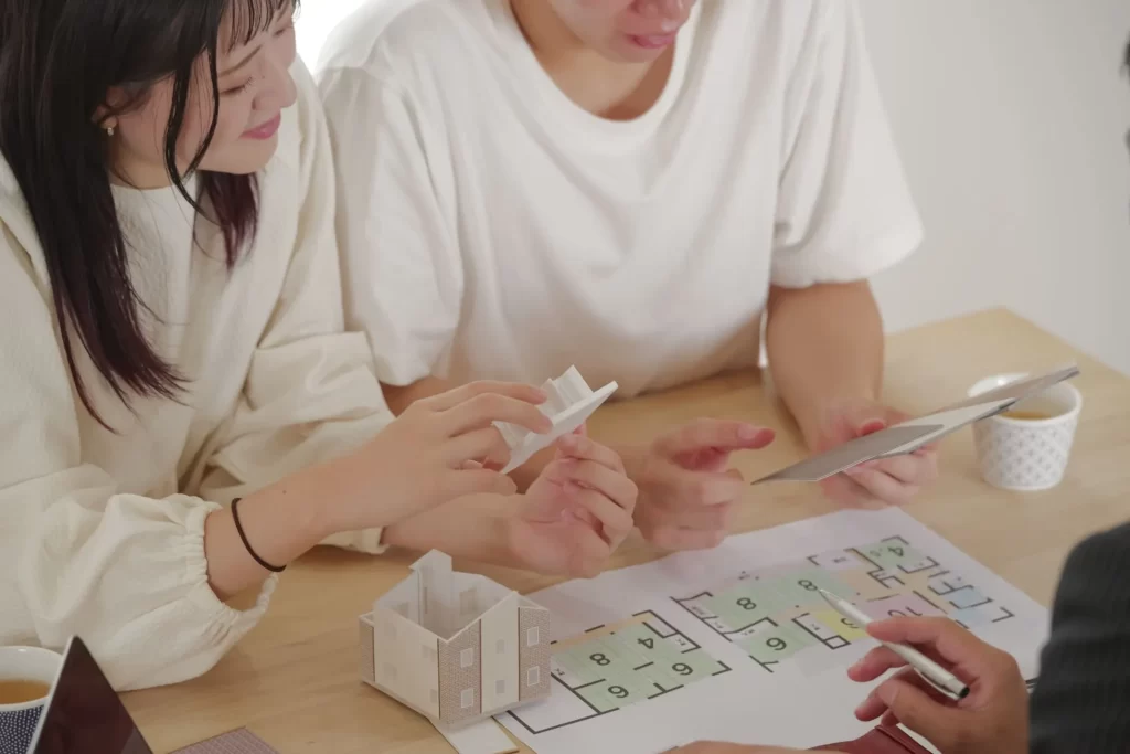 テーブルの上に置かれた住宅模型と図面を囲みながら、スタッフとご家族が土地選びや間取りについて相談している家づくり打ち合わせ風景。