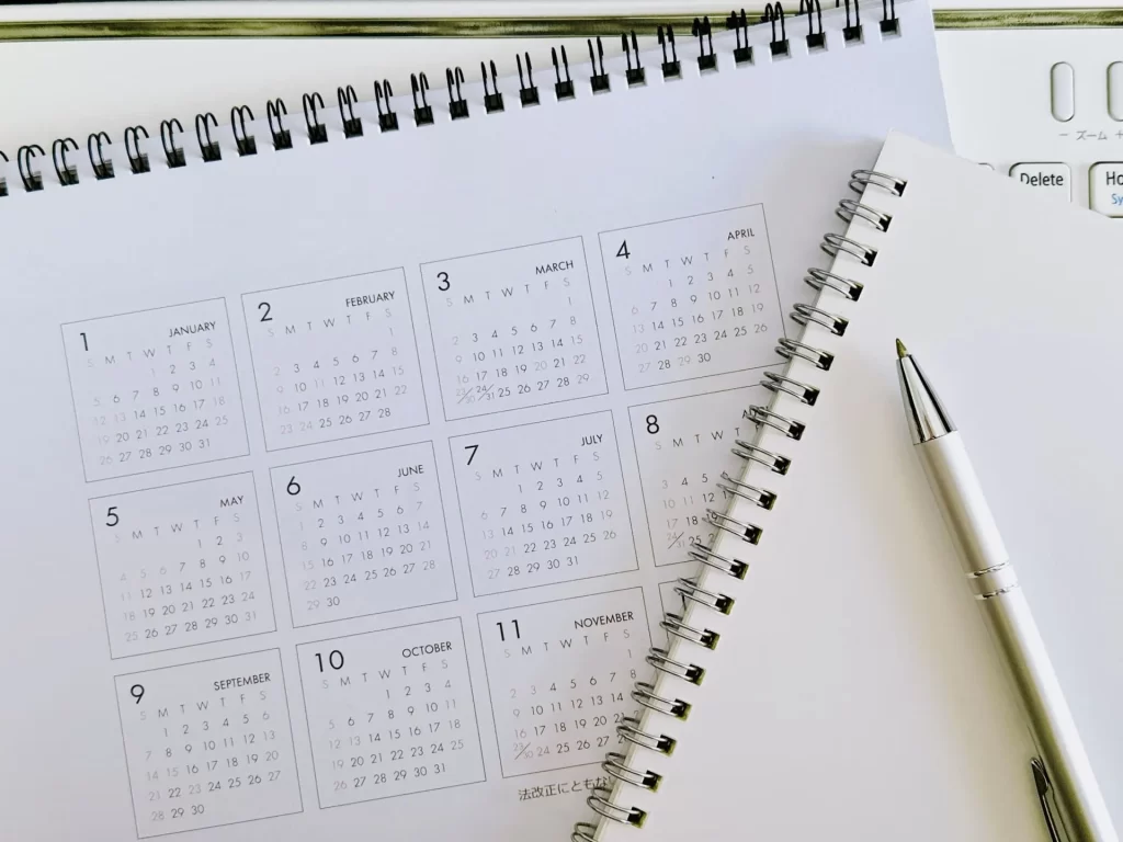 卓上カレンダーとリングノート、ボールペンが並び、注文住宅の着工から完成までの家づくりスケジュールを管理するイメージを表現した補助画像。