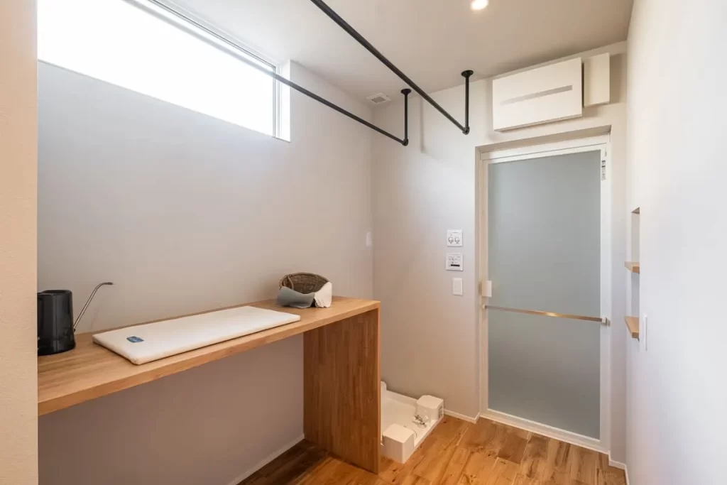 アイロン掛けができる作業カウンターと室内干し用のアイアンバーを設置した、家事動線に配慮した機能的で清潔感のある株式会社シンズクラフトのランドリールーム(家事室)。