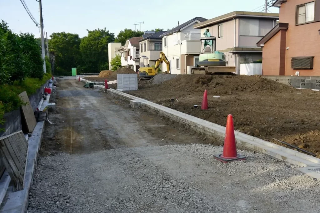 新しい住宅街の宅地造成工事が行われている風景で、ショベルカーによる土地の整地や境界ブロックの設置など、家を建てる前の土台作りが進む建築現場の様子。