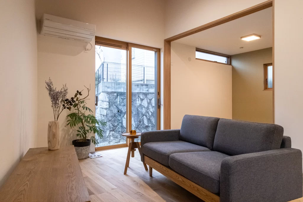 掃き出し窓から自然光が差し込む落ち着いた雰囲気のリビングで、グレーのソファと木製のローテーブル、観葉植物が配置された株式会社シンズクラフトの注文住宅の内観写真。