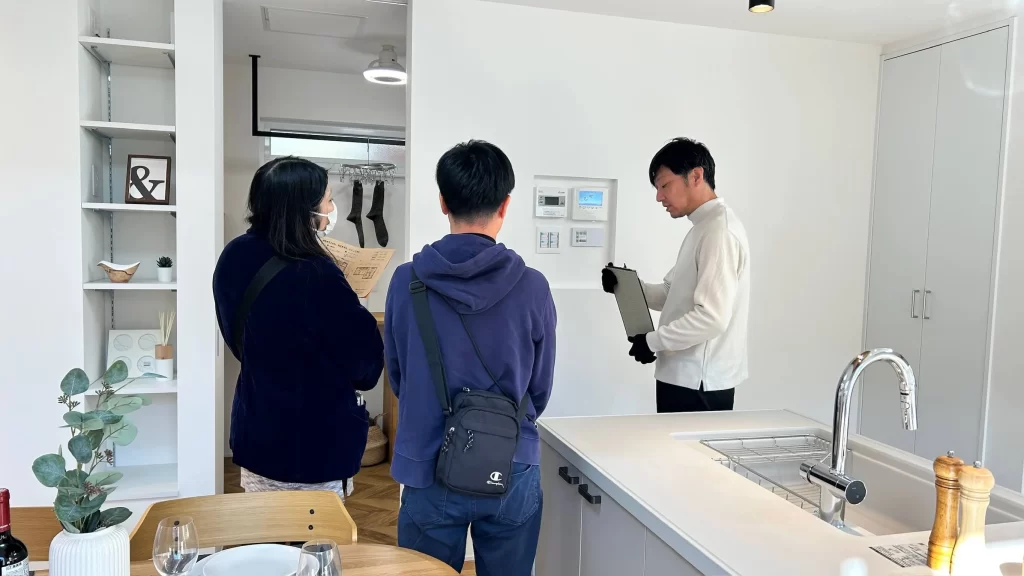 株式会社シンズクラフトの完成見学会にて、スタッフが施主様に住宅設備の操作方法や家づくりのこだわりを対面で丁寧に解説している、注文住宅のリアルな内覧シーンを収めた様子。