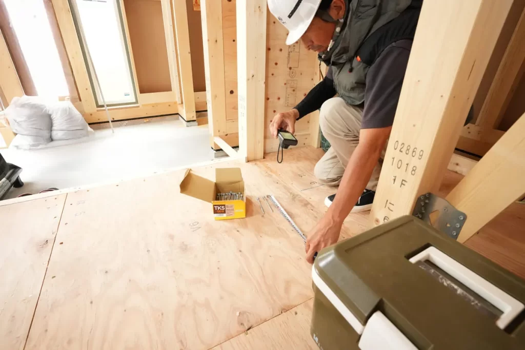 注文住宅の建築現場にて、ヘルメットを着用した技術者がメジャーを使って構造材の寸法を精密に計測・確認している、株式会社シンズクラフトの施工管理の様子。