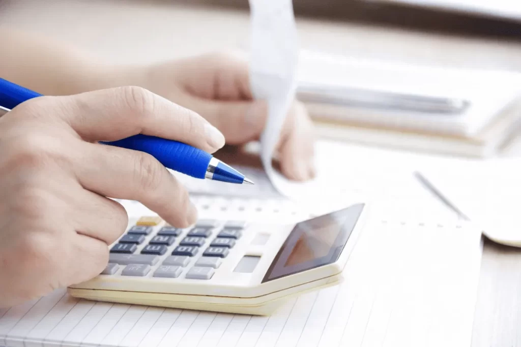 電卓とペン、書類を使いながら家づくりの総予算やローン返済計画について細かく計算を行っている手元の様子を写した、住宅購入における資金検討のイメージ写真。