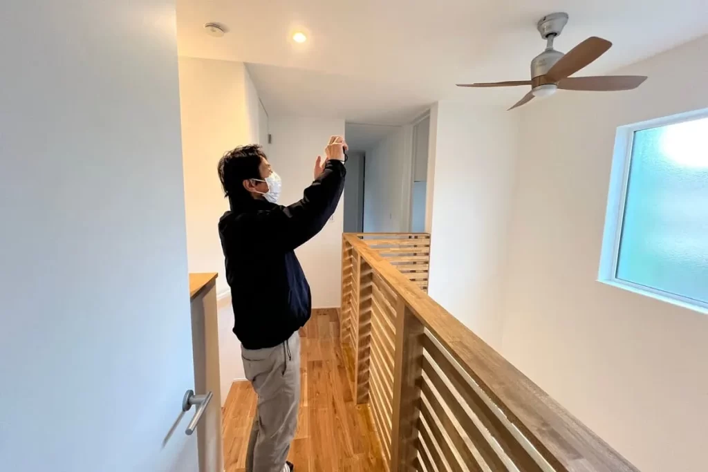 吹き抜けのある住宅の2階廊下で、シーリングファンを見上げながら点検・確認を行う様子。