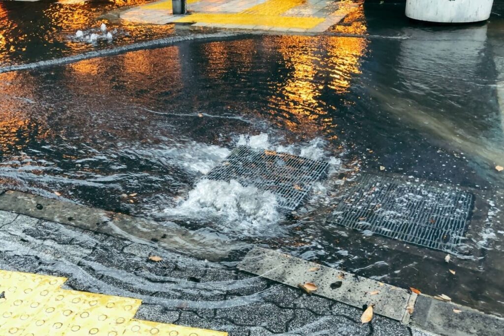 都市部の道路にある排水溝から、雨水が逆流して溢れ出している内水氾濫の現場写真。