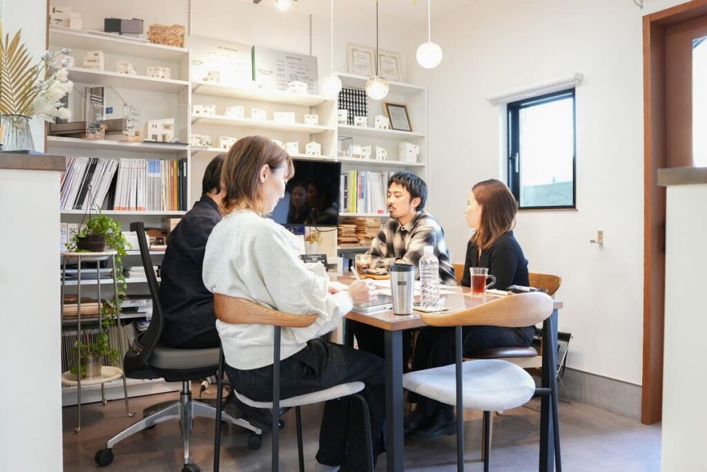模型やカタログが並ぶ打ち合わせスペースで、家づくりの相談を行うスタッフとお客様。