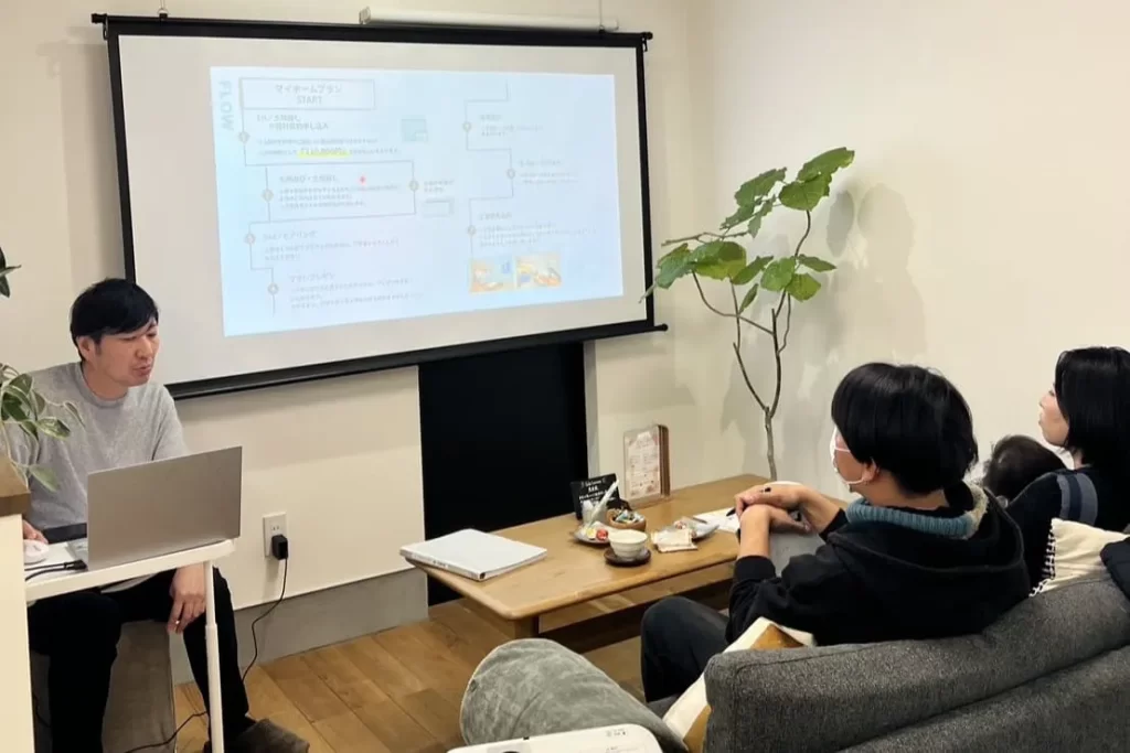 スクリーンを用いて、プロジェクターで資金計画や家づくりの流れを顧客に説明する相談会の風景。