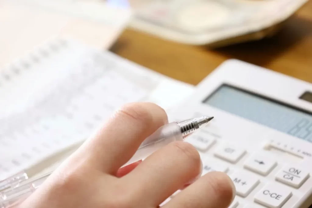 電卓とペンを持ち、家計や資金計画を立てる手元のクローズアップ。
