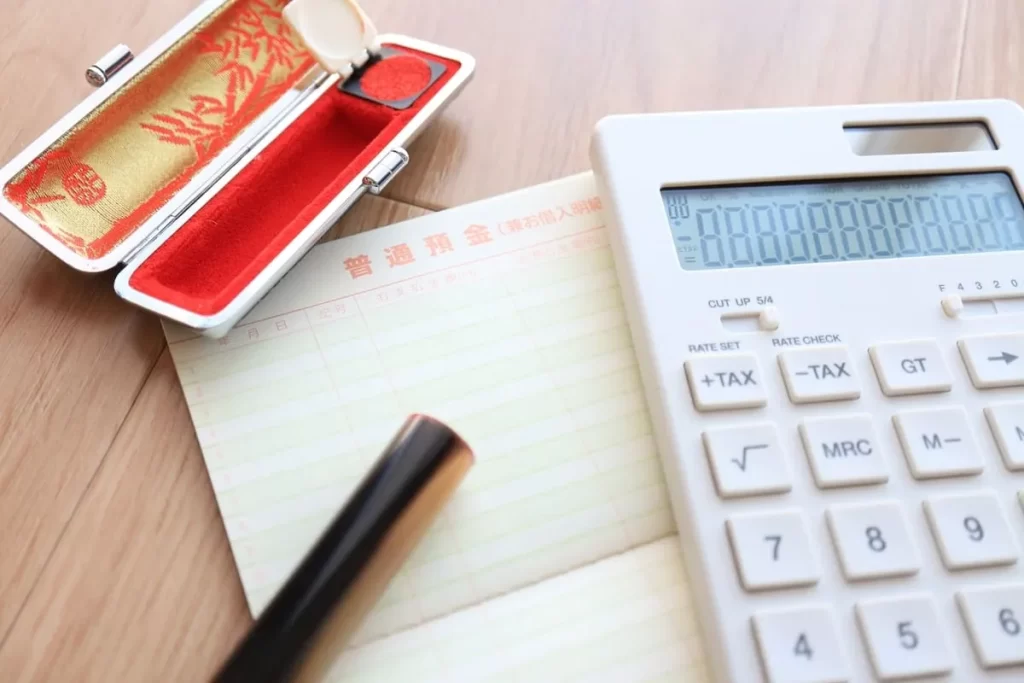 木目調のテーブルの上に置かれた普通預金通帳、印鑑、電卓のクローズアップ。