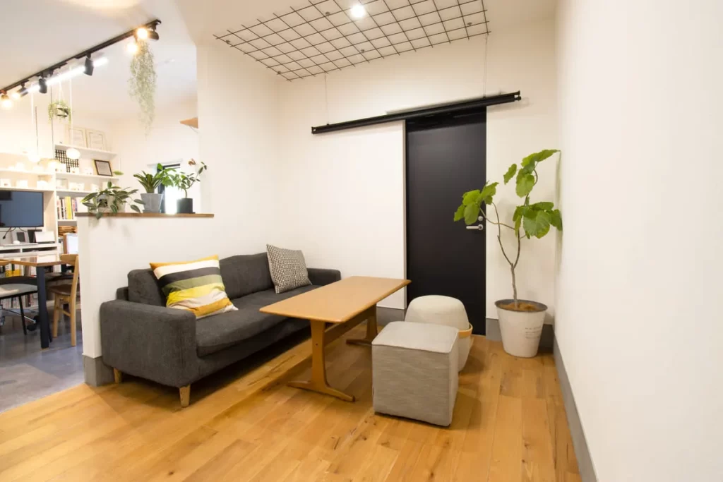 シンズクラフトの落ち着いた相談スペース。グレーのソファと木目のテーブル、観葉植物が配置された内装。