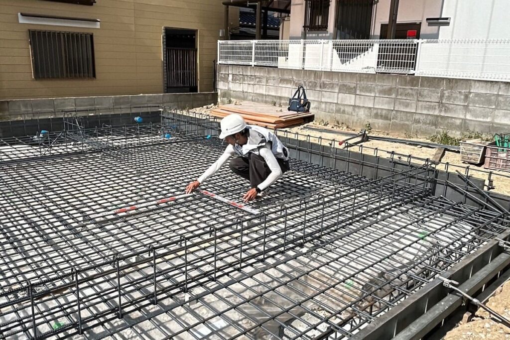 住宅の基礎工事現場で、職人が鉄筋の配筋検査を精密に行っている様子。