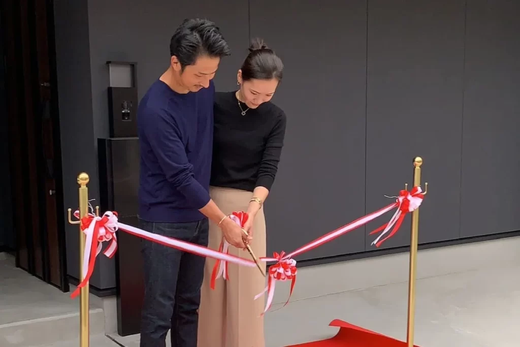 完成した新築住宅の前で、笑顔でテープカットを行う若い夫婦。