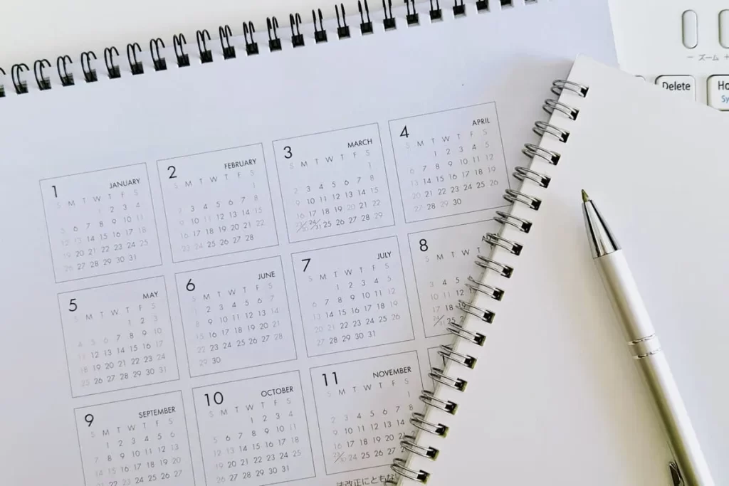 卓上カレンダーとノート、ペンが置かれたデスクの上。長期的な計画をイメージさせる構図。