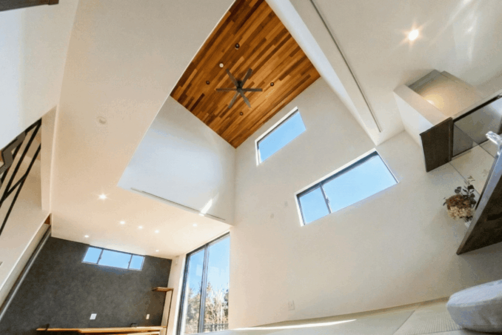 木目調の天井とシーリングファンが特徴的な、ダイナミックな吹き抜けがある狭小住宅の内観。