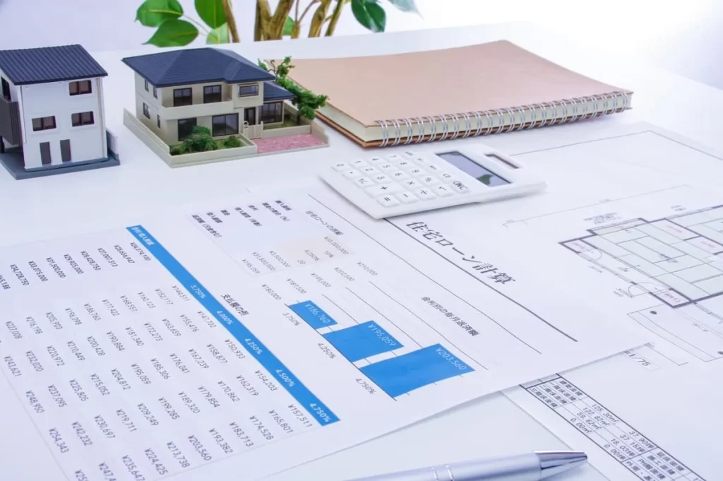 住宅ローンの計算書類、住宅模型、電卓、図面が整然と並べられた打ち合わせテーブルの様子。