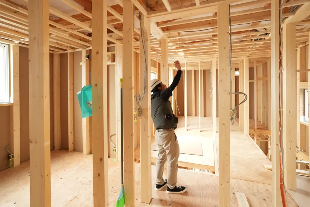 住宅の建築現場で、柱や梁の構造材を確認しながら作業を進める建築士。